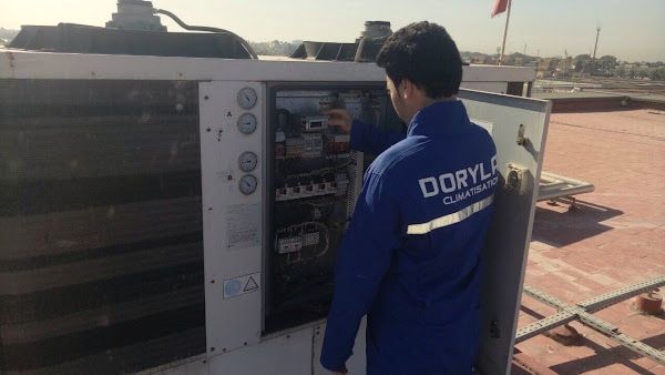 Technicien en tenue Dorylab vérifiant le tableau électrique d’une unité de climatisation en toiture