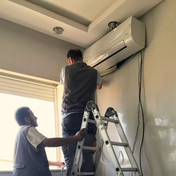 Deux techniciens intervenant sur un climatiseur mural, l’un monté sur un escabeau