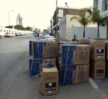 Cartons d’unités extérieures de climatisation livrés sur un trottoir, devant un immeuble de bureaux