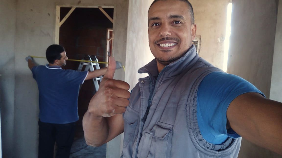 Technicien souriant, pouce levé, pendant qu’un collègue mesure un mur dans un bâtiment en chantier